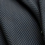 Close-up of authentic 1920s wool suiting fabric showing herringbone weave texture in charcoal gray, professional menswear detail photography, natural lighting highlighting fabric quality and craftsmanship