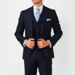 Sharp-dressed gentleman wearing navy three-piece 1920s suit with high button stance, white dress shirt, silk four-in-hand tie, polished oxford shoes, and charcoal fedora hat standing in classic vintage pose