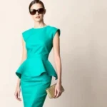 Fashion model wearing vibrant teal peplum dress with structured tailoring, standing confidently with oversized sunglasses and metallic gold handbag, against neutral backdrop showing 2010 haute couture style