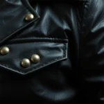 Close-up of distressed black leather jacket with metal studs and chains, worn texture visible, dramatic lighting against dark background, photorealistic