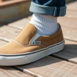 Vintage Vans slip-on sneakers worn with white crew socks on weathered wooden skateboard ramp, natural daylight, close-up detail shot showing canvas texture and iconic silhouette