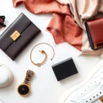 Overhead flat lay of luxury fashion items arranged artfully: designer sunglasses, gold jewelry, leather wallet, silk scarf, and white sneakers on marble background with soft natural lighting