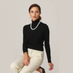 Woman wearing classic black turtleneck sweater, cream tailored trousers, ballet flats, pearl necklace, minimal accessories, sophisticated neutral palette, posed elegantly, professional fashion photography