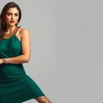 Fashion-forward woman wearing jewel-toned emerald green fitted dress with statement gold jewelry and metallic heels, confident pose against neutral background, professional fashion photography