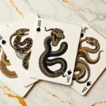 Luxury Year of the Snake playing cards spread artistically on marble surface with gold accents, showcasing intricate snake illustrations and metallic finishes in fashion editorial style photography