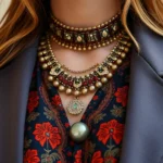 Close-up of expertly styled 1970s bohemian blouse layered under modern structured blazer with contemporary jewelry, photorealistic fashion detail shot