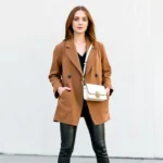 Woman wearing oversized vintage blazer styled with black leather pants, white minimalist sneakers, and contemporary crossbody bag, standing against neutral urban backdrop, natural daylight, confident expression, modern styling aesthetic