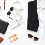 Professional fashion flat lay featuring classic tailored pieces, white button-down shirt, black blazer, neutral accessories, and quality leather bag arranged on white background, sophisticated and timeless aesthetic