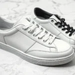 Luxury leather designer sneakers in pristine white and black, displayed on marble surface with minimalist aesthetic, professional product photography style, high-end footwear showcase