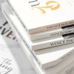 Flat lay of luxury fashion books with elegant typography and gold accents stacked on white marble surface, soft natural lighting, close-up detail shot