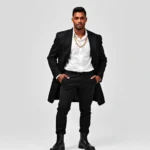 Confident person wearing oversized black blazer with white crisp shirt, tailored black trousers, polished black leather boots, chunky gold chain necklace, standing against minimal background with powerful posture