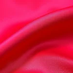 Close-up of vibrant pomegranate red silk fabric with subtle texture, professional fashion photography style, natural lighting highlighting deep crimson tones and luxurious sheen