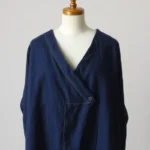 Minimalist Japanese vintage indigo cotton garment with asymmetrical neckline displayed on neutral background, showcasing fine hand-stitched seams and natural fabric texture, soft studio lighting highlighting craftsmanship details