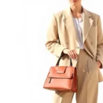 Minimalist fashion styling with oversized tailored blazer in neutral beige, paired with high-waisted trousers and structured leather handbag, photographed in natural daylight against soft white background