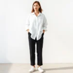 Woman in minimalist monochromatic outfit: white oversized linen shirt, tailored black trousers, white sneakers, standing against neutral background, natural morning light, serene expression