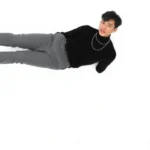 Asian male model wearing perfectly fitted black turtleneck tucked into high-waisted gray tailored trousers, cropped to ankle length, paired with white minimalist leather sneakers and delicate silver chain necklace, standing against neutral white background in confident pose