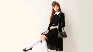 A young woman wearing a Classic Lolita coordinate with a black JSK dress, white knee-high socks, black Mary Jane shoes, an ornate headbow, and a structured lace bag, posing elegantly in soft natural lighting with a neutral background.