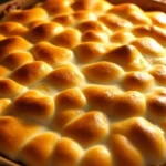 Golden-brown marshmallow topped sweet potato casserole fresh from the oven, creamy filling visible at edges, warm autumn lighting, rustic ceramic baking dish