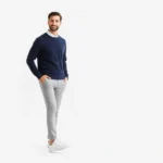 Well-dressed man in coordinated neutral outfit consisting of fitted navy sweater, light gray chinos, and classic white sneakers, standing confidently against minimalist white background, natural daylight, lifestyle photography, approachable masculine style