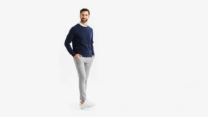 Well-dressed man in coordinated neutral outfit consisting of fitted navy sweater, light gray chinos, and classic white sneakers, standing confidently against minimalist white background, natural daylight, lifestyle photography, approachable masculine style