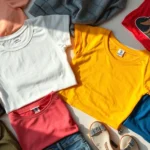 Overhead flat lay of colorful Shein clothing items including crop tops, printed tees, and trendy pieces arranged artfully with natural lighting, showing texture and fabric details