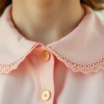 Close-up of vintage Peter Pan collar blouse in soft pink with delicate lace trim, worn with small gold brooch, pastel aesthetic, natural daylight, detailed fabric texture