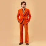 Man wearing vintage 1970s wide-lapel blazer in burnt orange with matching flared trousers and platform shoes, standing confidently against neutral background, warm studio lighting emphasizing fabric texture and fit