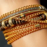 Professional close-up of layered delicate gold chains and chunky mixed-metal bracelets stacked on a wrist, showcasing texture and contrast, natural lighting emphasizing shine and craftsmanship details