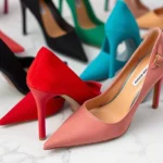 Close-up of Fashion Nova high-heeled shoes in multiple colors arranged on white marble surface, showing heel details and shoe variety, professional product photography style