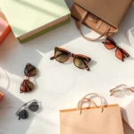 Overhead flat lay of fashion shopping bags in neutral and pastel colors on marble floor with sunglasses and designer accessories artfully arranged, bright natural lighting