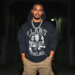 Black oversized hoodie layered over a vintage band tee, styled with cargo pants and chunky silver chains, worn by a man standing confidently against a dark urban backdrop with moody lighting