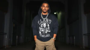 Black oversized hoodie layered over a vintage band tee, styled with cargo pants and chunky silver chains, worn by a man standing confidently against a dark urban backdrop with moody lighting