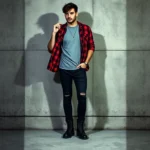 Man wearing distressed black skinny jeans, oversized gray band t-shirt, open red plaid flannel shirt, black combat boots, standing against concrete wall with moody lighting, confident relaxed posture