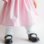 Close-up of pastel pink and blue babydoll dress with puffed sleeves, styled with black Mary Jane platform shoes and white leg warmers, shot against soft white background