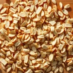 Close-up overhead view of scattered old fashioned oat flakes on natural wood surface with morning sunlight, showing texture and individual flat pieces clearly, warm neutral tones, no text or labels visible