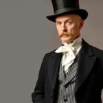 Distinguished Victorian gentleman in formal black morning coat with striped trousers, white dress shirt with high collar, silk cravat, and top hat, photographed in professional studio setting with neutral background, showcasing impeccable tailoring and refined posture characteristic of 1880s formal daytime wear