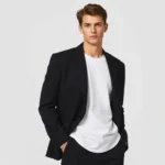 Model wearing oversized black blazer with white t-shirt and straight-leg black trousers, standing against neutral background, confident minimalist aesthetic, professional fashion photography