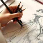 Woman holding colored pencils over an intricate fashion illustration of an elegant evening gown with flowing fabric details and ornate patterns, soft natural lighting, creative workspace aesthetic, photorealistic