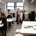 Fashion design studio in NYC's Garment District with sketching tables, mood boards, and young designers collaborating on seasonal collection designs
