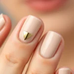 Close-up of elegant minimalist nail art featuring neutral beige base with single metallic gold geometric accent on middle finger, professional manicure on well-groomed hands, soft studio lighting, shallow depth of field, luxury aesthetic