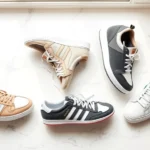 Flat lay of five premium designer sneakers arranged artfully on white marble surface, showcasing different silhouettes and materials including leather, suede, and canvas in neutral and bold colorways, natural window lighting