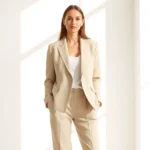 Woman in neutral beige linen blazer and tailored trousers standing confidently in bright natural light, minimalist aesthetic, professional styling, high-quality fabrics visible, natural lighting emphasizing texture and craftsmanship