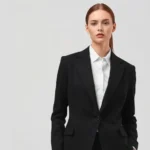 Minimalist fashion model wearing tailored black blazer and white shirt, neutral background, professional studio lighting emphasizing garment construction details and fabric texture